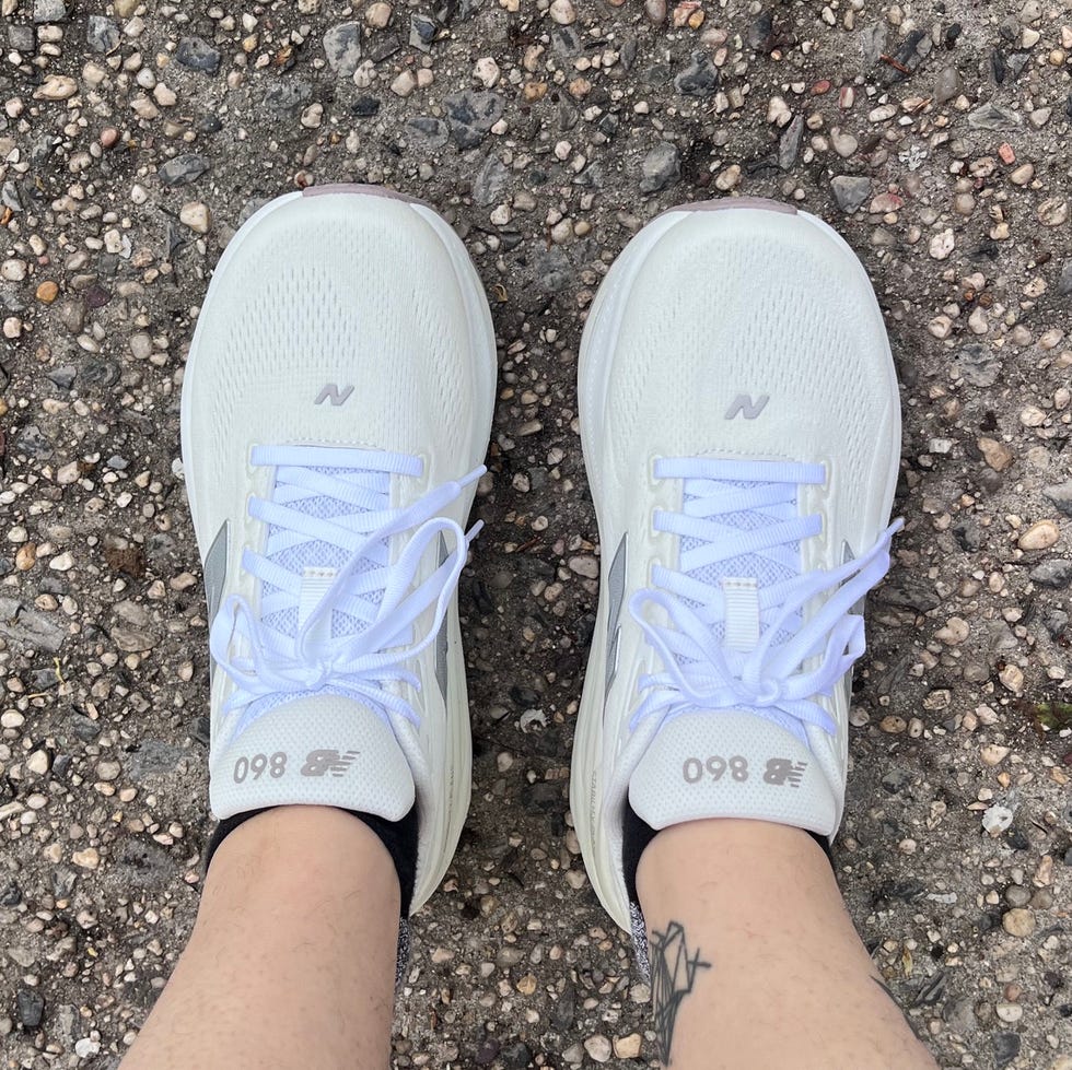 White New Balance sneakers worn with black ankle socks on a gravel surface.