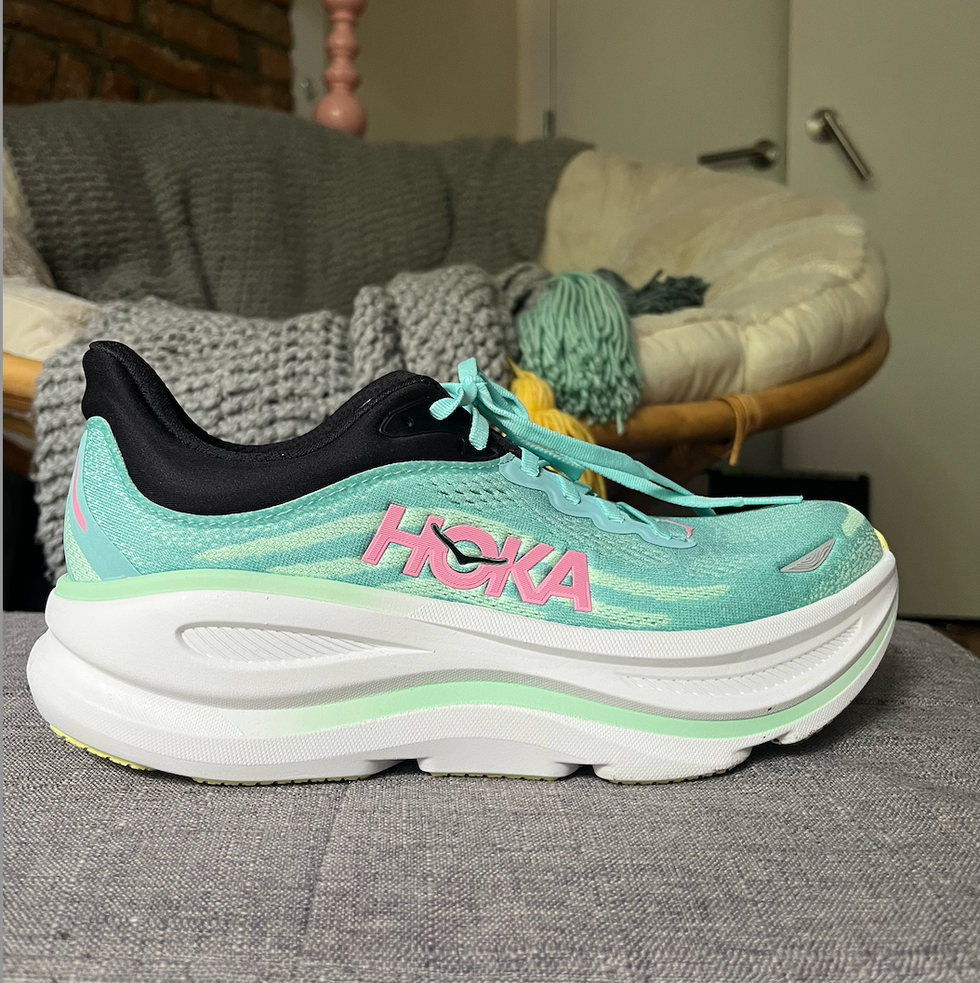 A side view of a light blue running shoe with pink accents from the brand HOKA.