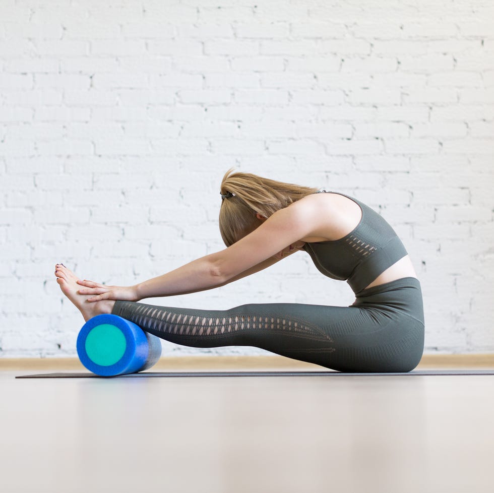 Attractive woman doing typical stretching, head to knees with foam blue roller, paschimottanasana pose, indoor at club attractive woman doing typical stretching, head to knees with foam blue roller, paschimottanasana pose, indoor at club