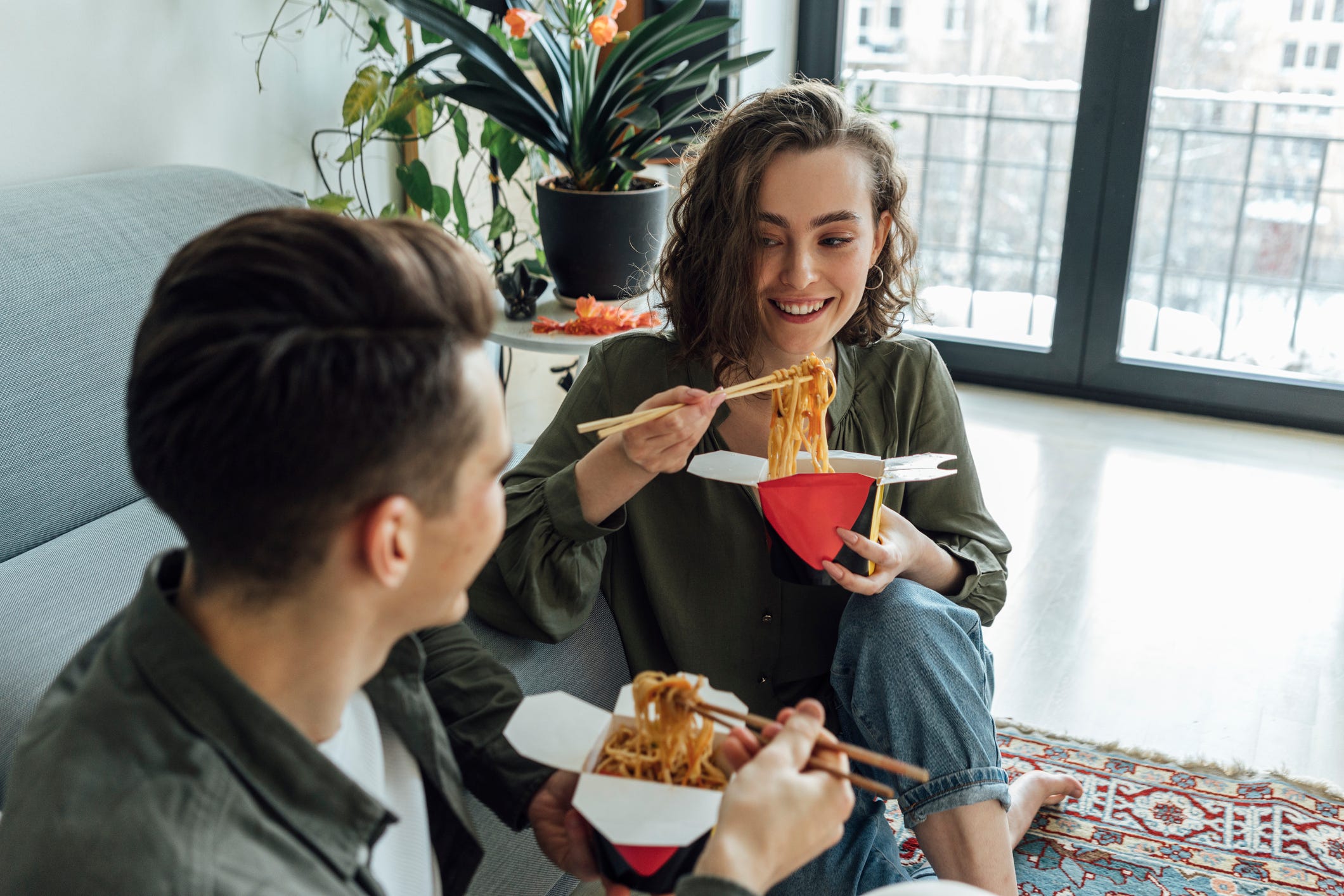 Happy woman and man with take out food talking in living room at home
