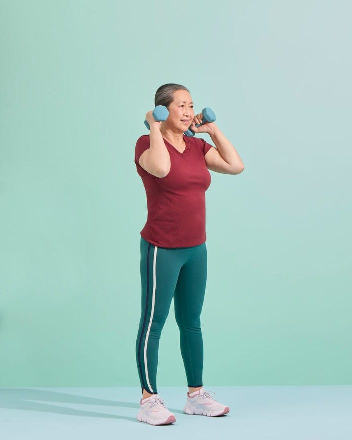 Woman exercising with dumbbells, wearing a maroon shirt and teal leggings against a mint green background.