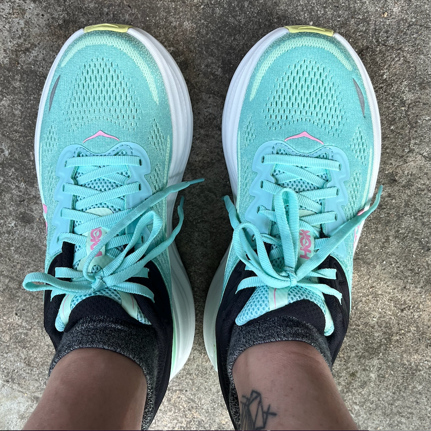 Sporty mint green sneakers with black accents and laces, worn on a concrete surface.