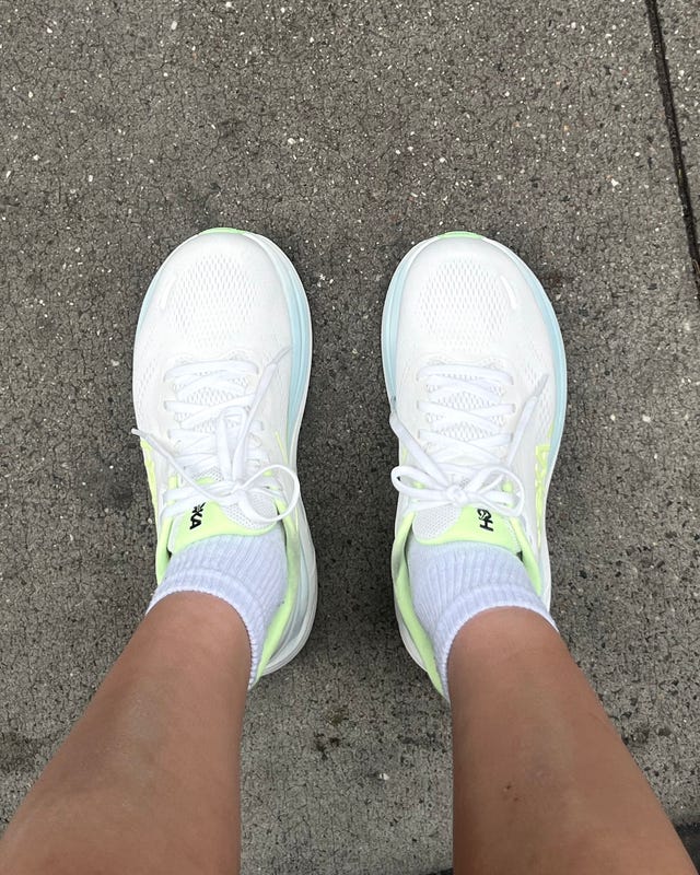 A pair of white athletic shoes with neon accents, worn with white socks on a concrete pavement. A pair of white athletic shoes with neon accents, worn with white socks on a concrete pavement.