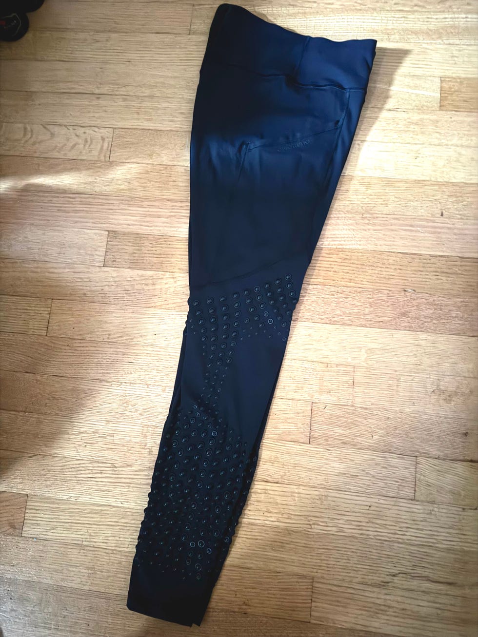 Black leggings with textured detailing and pockets, laid flat on a wooden surface.