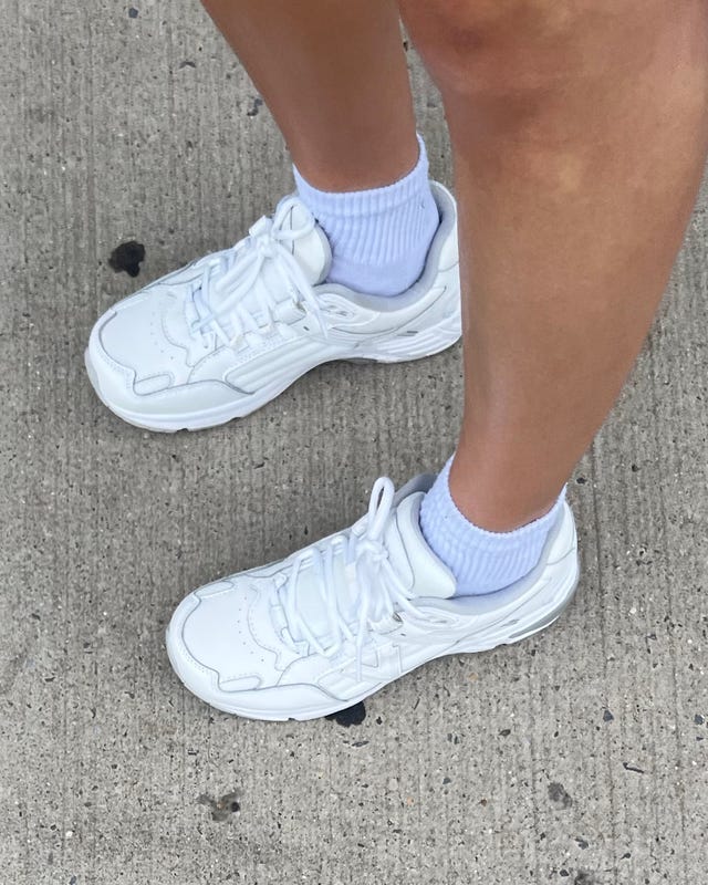 White athletic shoes worn with light blue ankle socks on an outdoor surface.