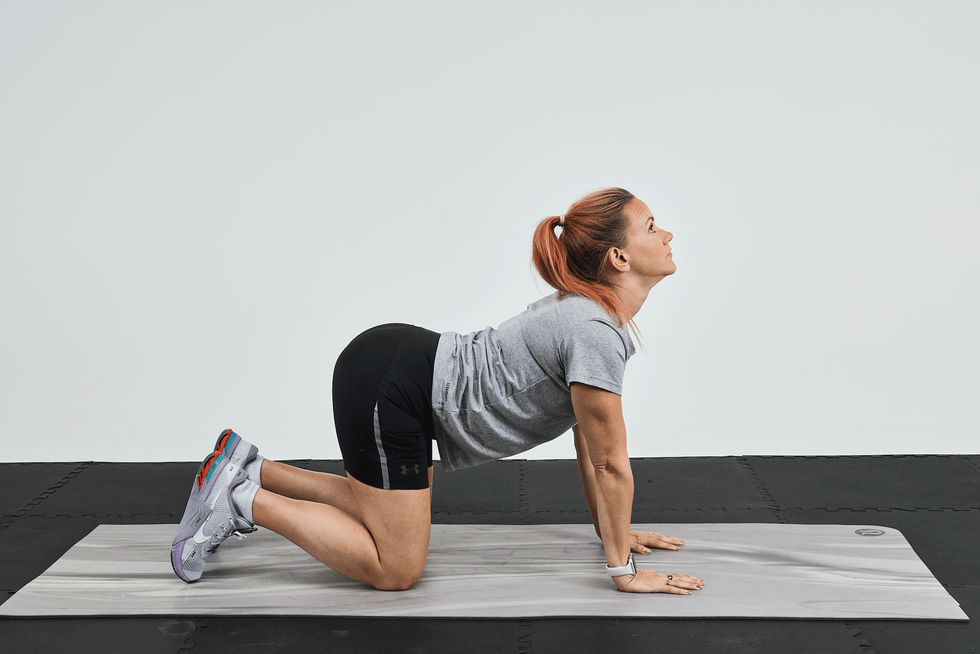 Woman performing a yoga pose on a mat, with her back arched and head tilted upward.