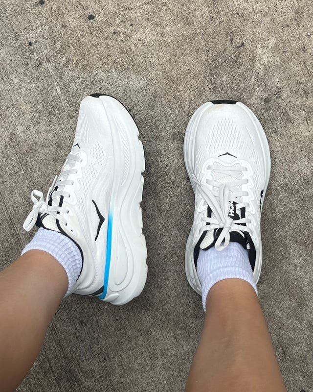 Close-up of two white athletic shoes on a concrete surface, with blue accents and white socks.