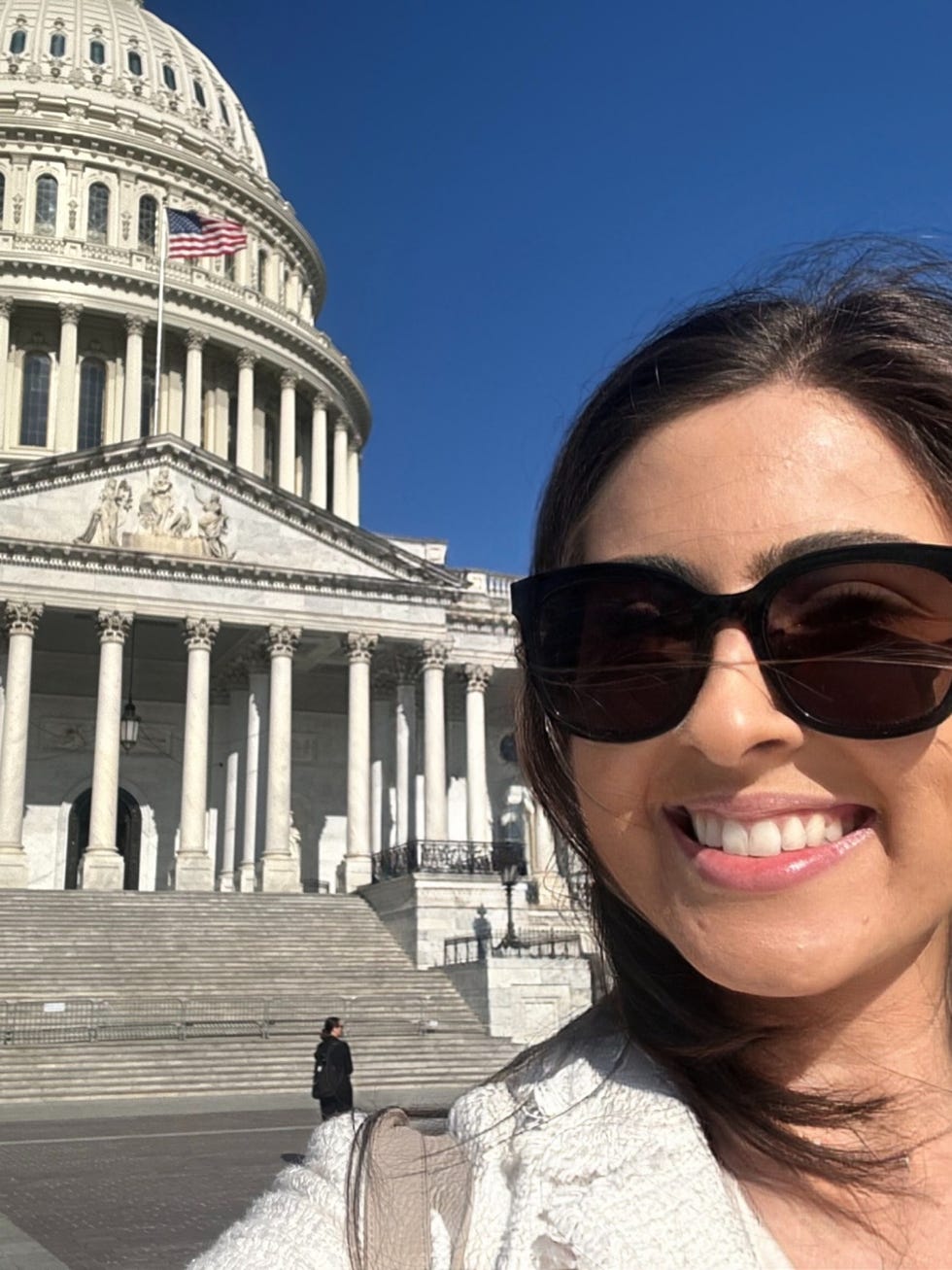 Smiling person in sunglasses in front of the U.S. Capitol building on a sunny day.