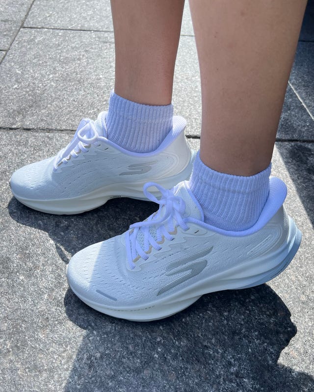 Close-up of white athletic shoes worn with light-colored ankle socks standing on a stone pavement. Close-up of white athletic shoes worn with light-colored ankle socks standing on a stone pavement.
