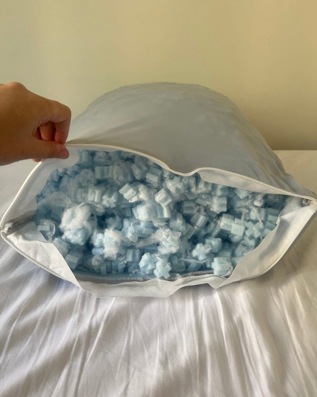A hand opening a pillow revealing light blue filling inside a white cover on a bed.