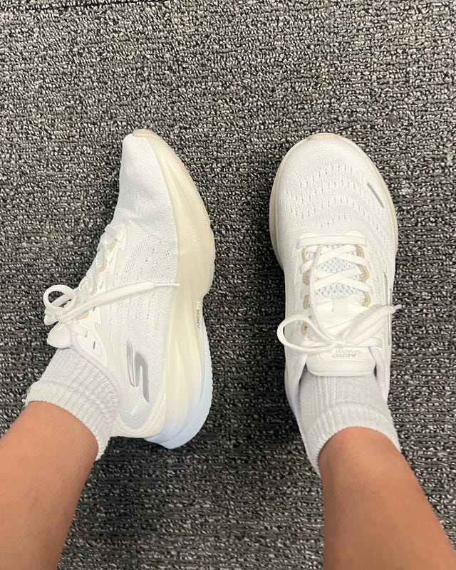 White athletic shoes worn with gray ankle socks, viewed from above on a carpeted floor. White athletic shoes worn with gray ankle socks, viewed from above on a carpeted floor.