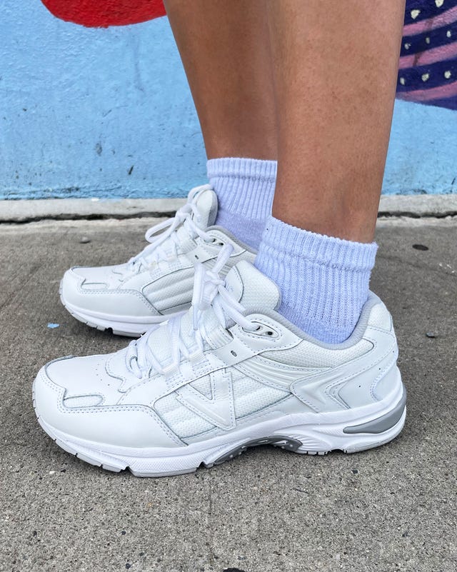 White athletic shoes paired with light socks on a concrete surface.