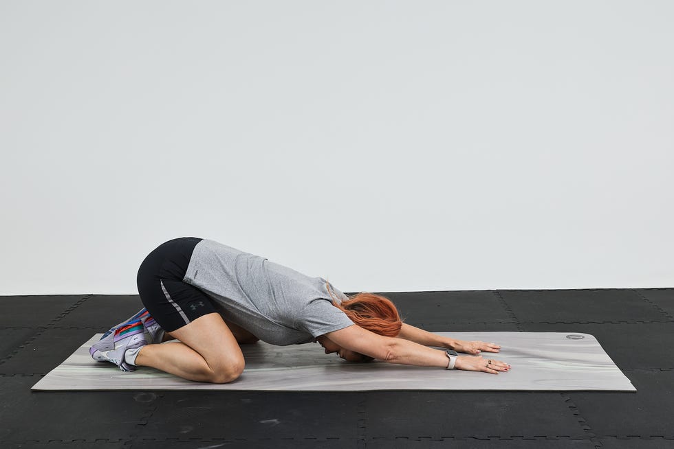 A person performing a yoga pose on a mat, with arms extended forward and knees on the ground.