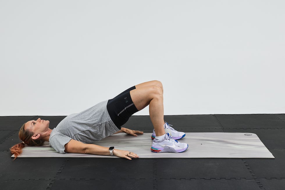 Person performing a bridge exercise on an exercise mat with a gray background.