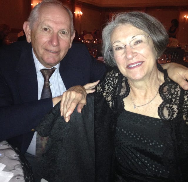 A couple smiling together at a formal event, with elegant attire and ambient lighting in the background.