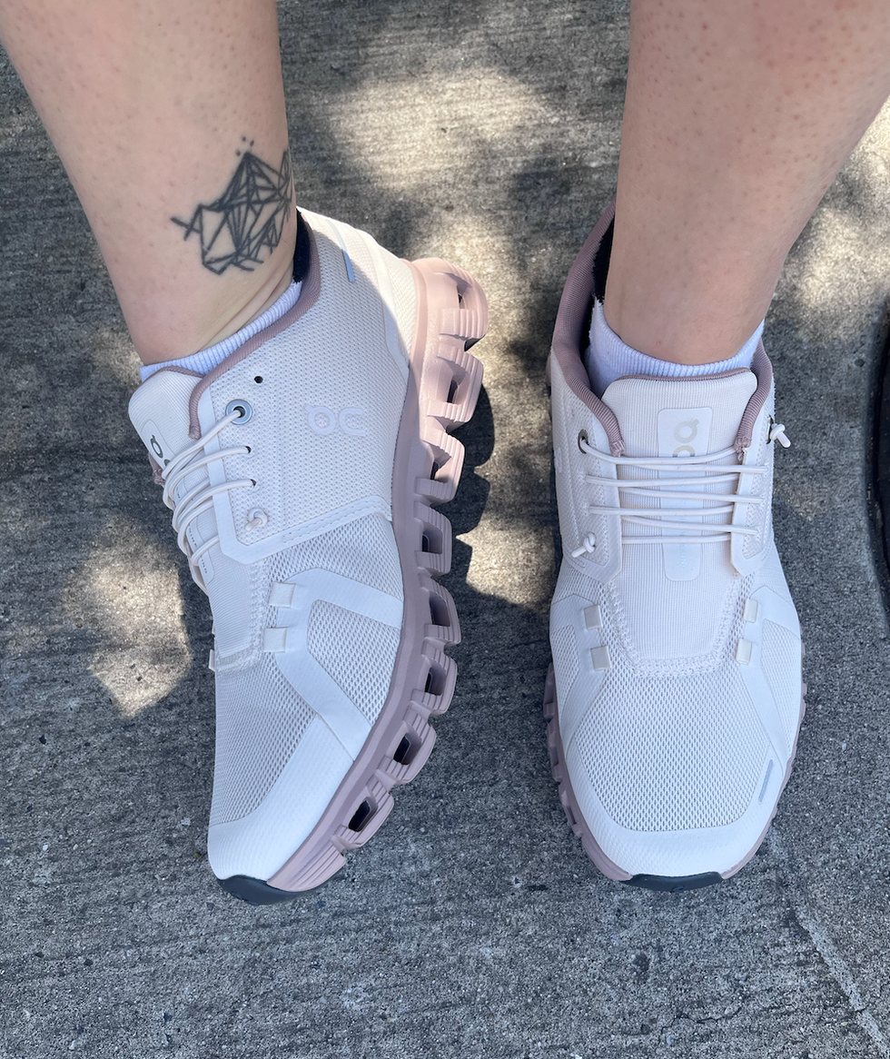 Light pink athletic shoes worn on feet with a geometric tattoo visible on the ankle.