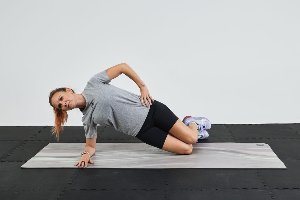 A woman performing a side plank exercise on a gym mat.