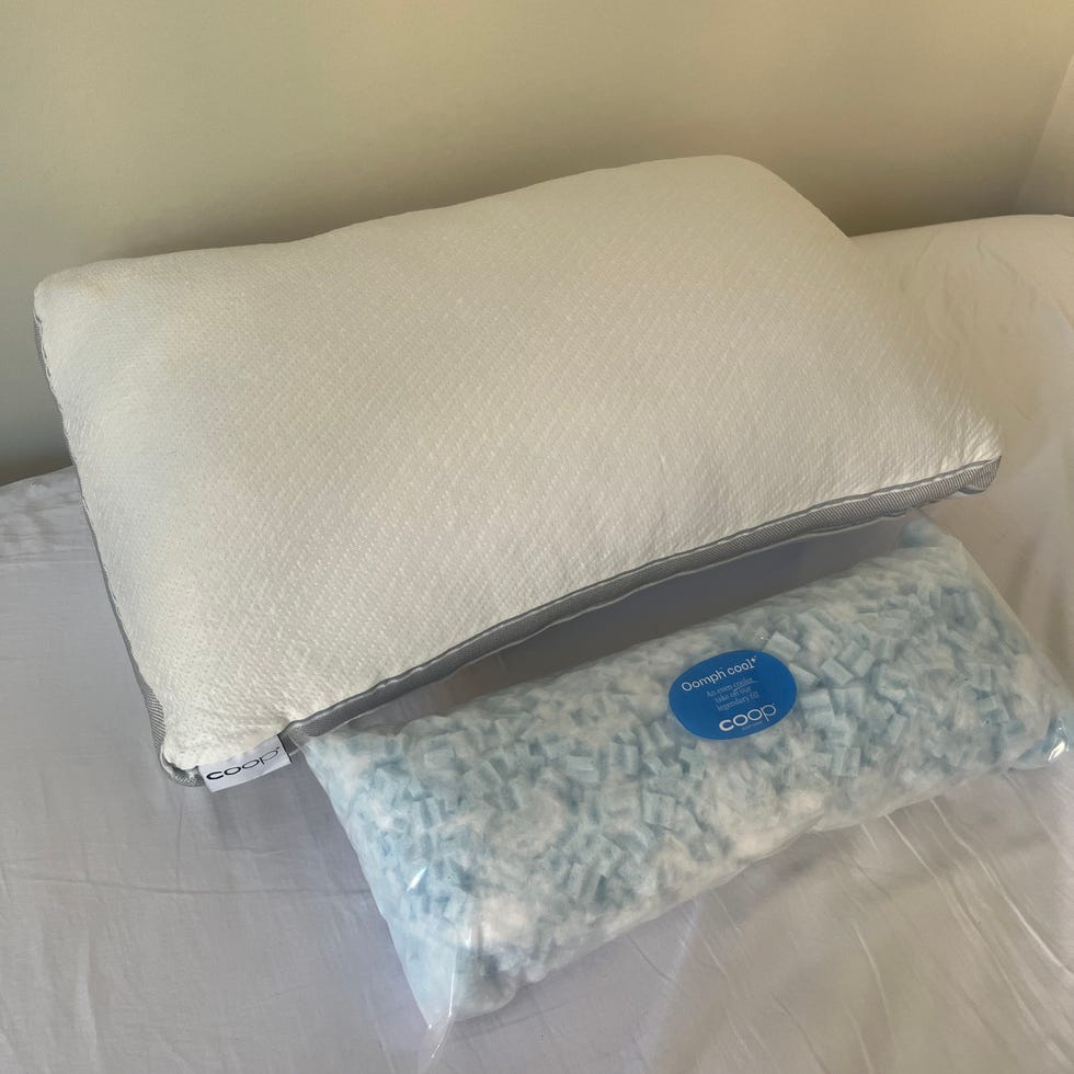 A white pillow on a bed next to a packaged pillow filled with blue foam pieces.