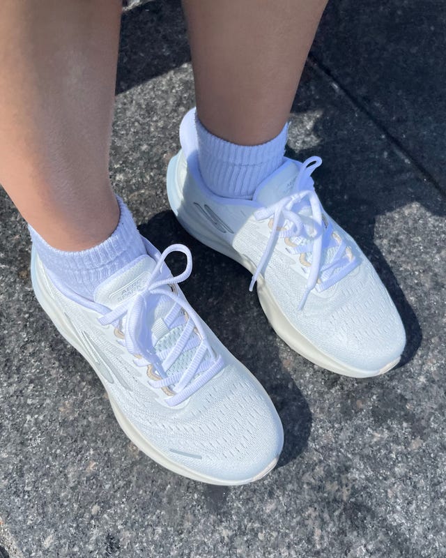 White athletic shoes paired with white crew socks on a person's feet, standing on a stone surface. White athletic shoes paired with white crew socks on a person's feet, standing on a stone surface.