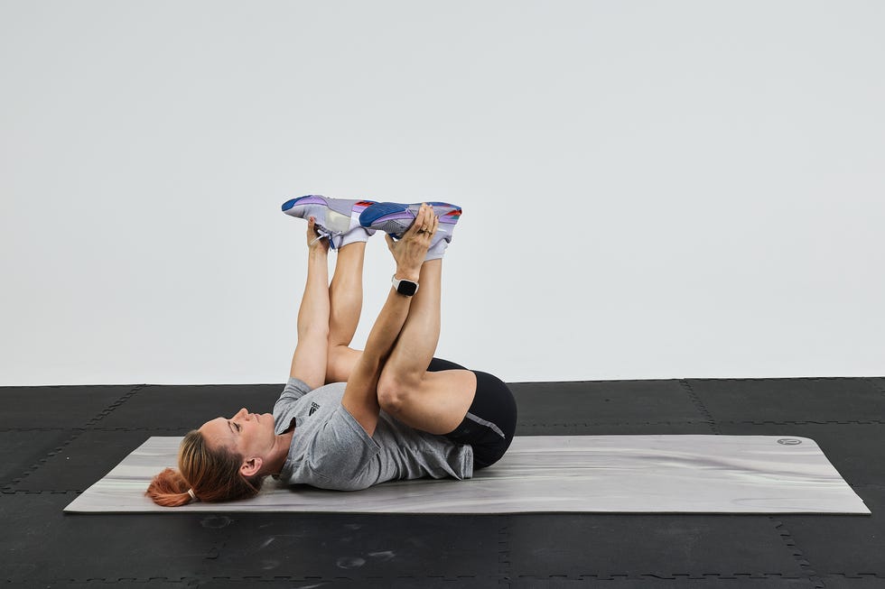 Person performing a stretching exercise on a mat, holding their legs above their head.