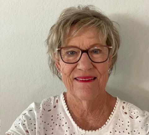 Smiling woman with short hair and glasses, wearing a white top against a plain background.