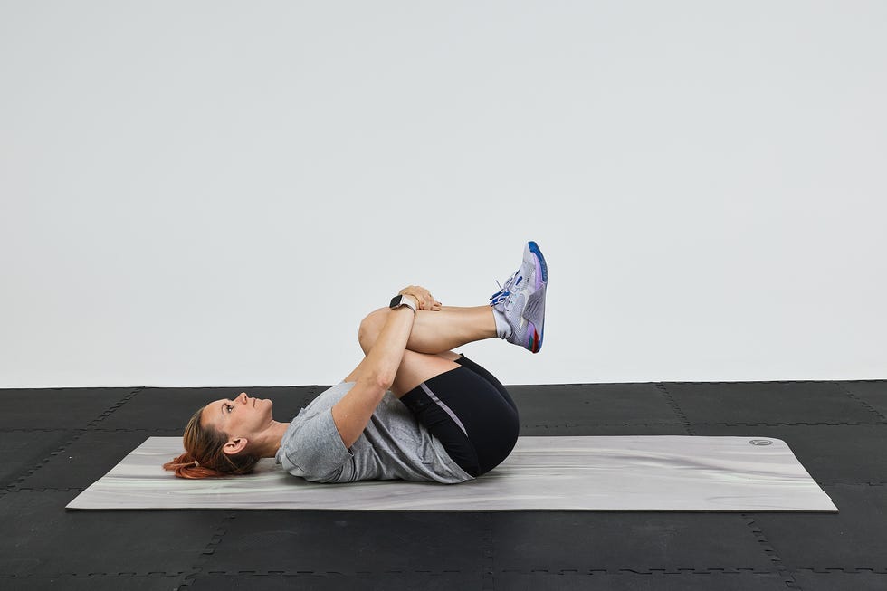 A person demonstrating a stretch on a yoga mat, holding their knees close to their chest.