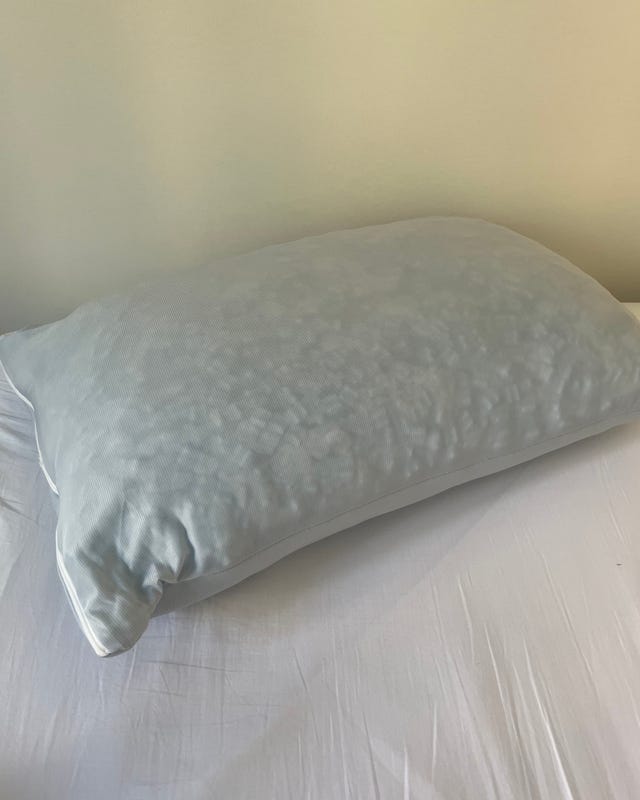 Light blue pillow resting on a white bed sheet against a plain wall.
