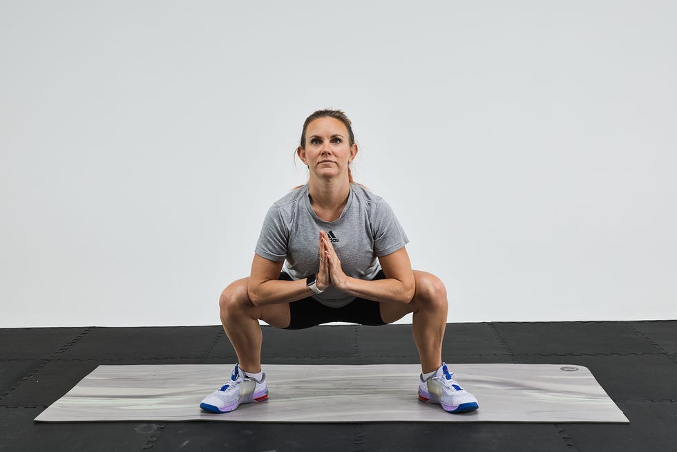 Woman performing a squat on an exercise mat with hands in prayer position, focused and engaged.