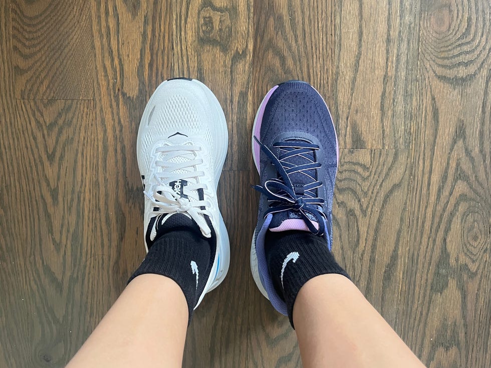 A pair of mismatched athletic shoes, one white and one dark navy, worn with black socks on a wooden floor.