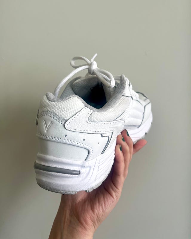White athletic shoe held in a hand, showcasing the back view with a tied shoelace.