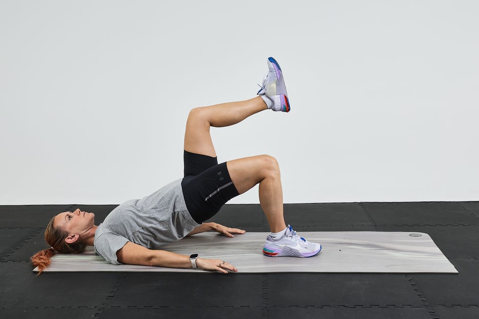A person performing a single-leg bridge exercise on a mat in a gym setting.