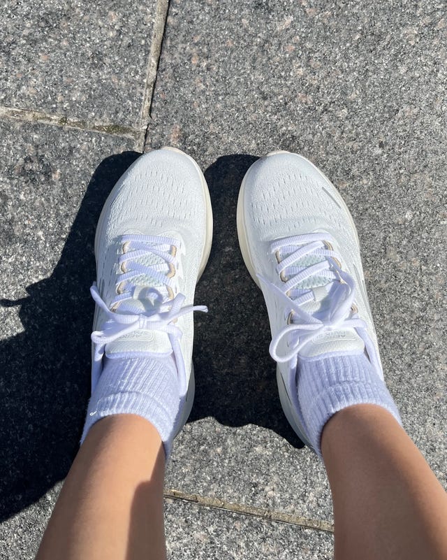 White athletic shoes paired with light-colored socks, resting on a textured stone surface. White athletic shoes paired with light-colored socks, resting on a textured stone surface.