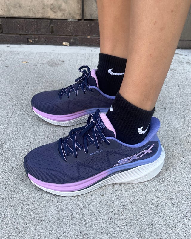 Navy and pink athletic shoes worn with black socks, positioned on a sidewalk with a textured background.