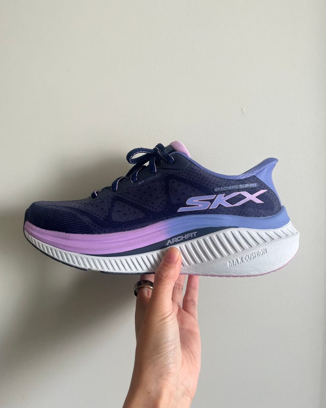 A navy and purple Skechers running shoe held by a hand against a neutral background.