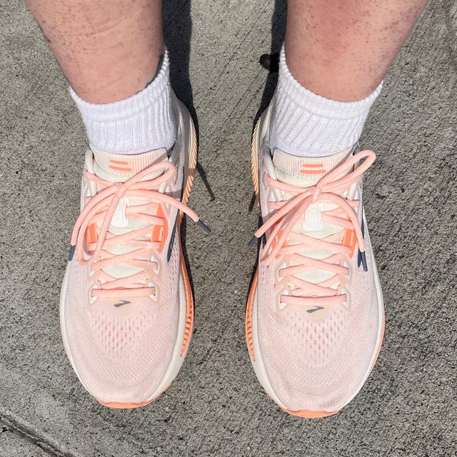 Light pink running shoes with white socks on a concrete surface.