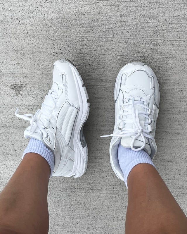 White sneakers worn with light socks on a concrete surface.