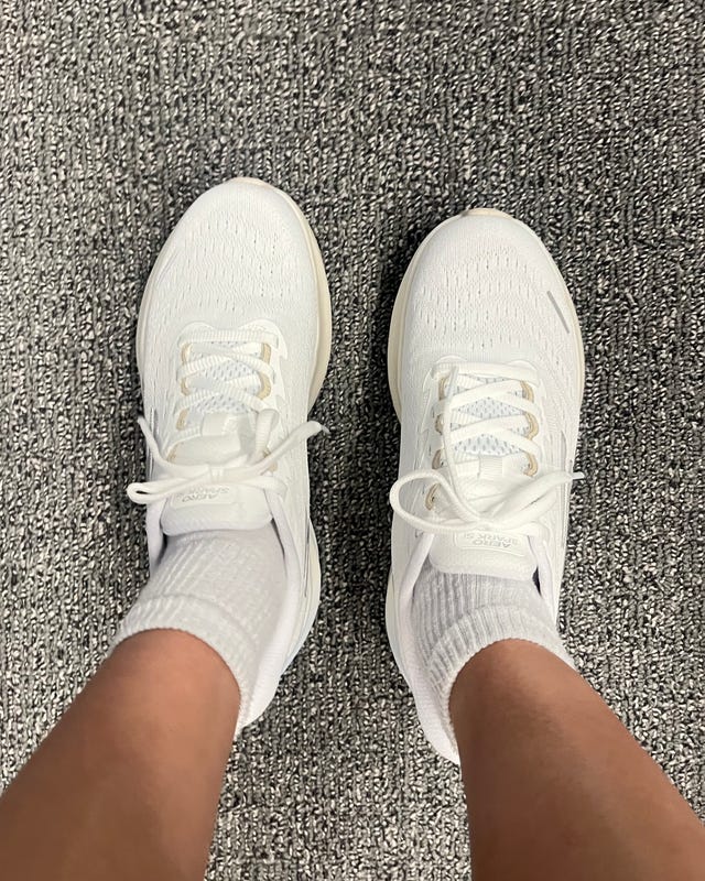 White athletic shoes worn with white socks on a textured gray floor. White athletic shoes worn with white socks on a textured gray floor.