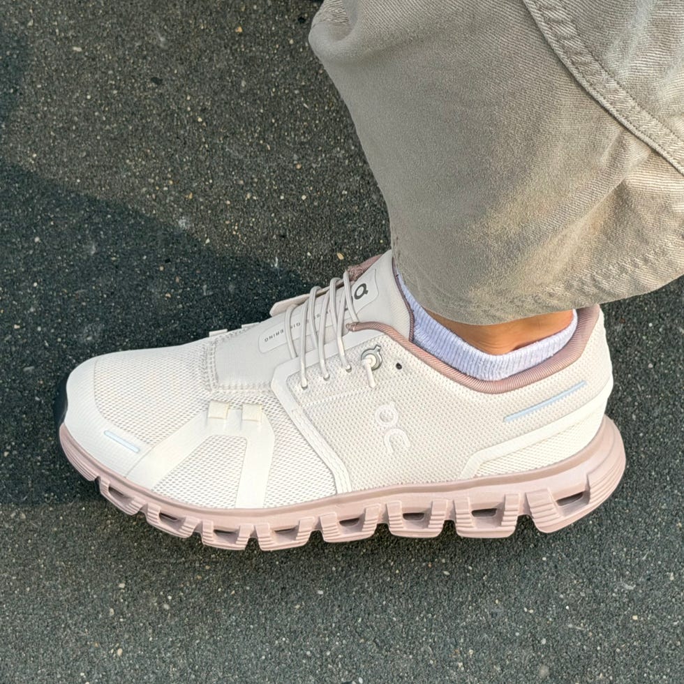 Light-colored sporty sneaker on a person’s foot, standing on a textured surface.
