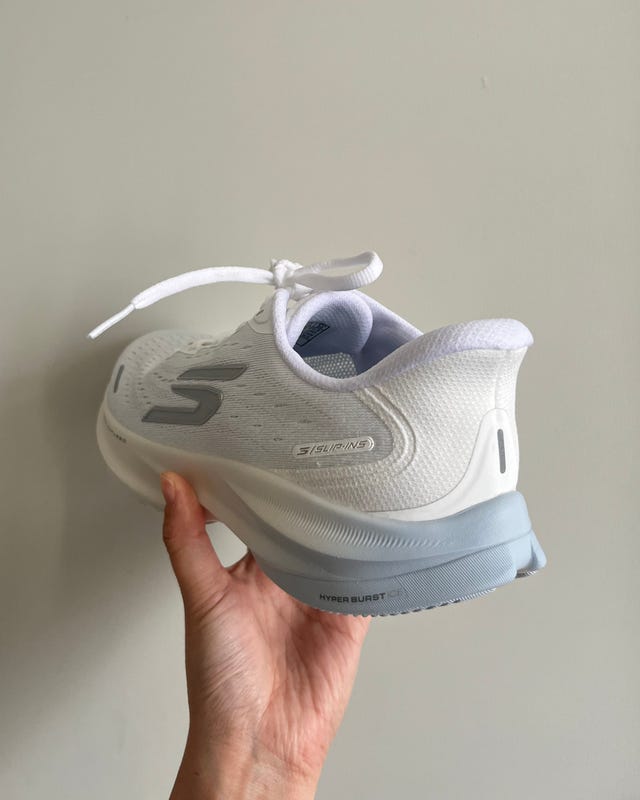 White athletic shoe held in hand, featuring a mesh upper and a light blue sole. White athletic shoe held in hand, featuring a mesh upper and a light blue sole.