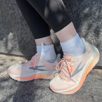 A person wearing athletic leggings and light-colored sneakers with a gradient sole, seated on a stone surface.