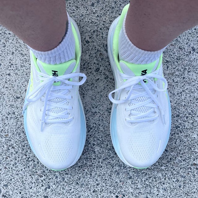 White athletic shoes with neon yellow accents on a person’s feet, resting on a concrete step.