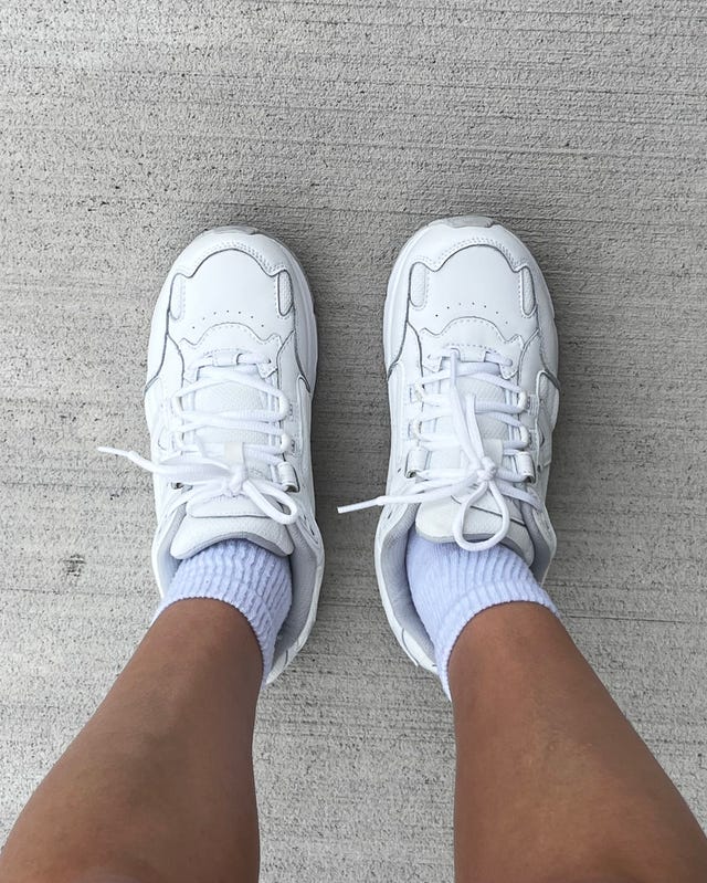White sneakers and light socks on bare feet, standing on a gray concrete surface.