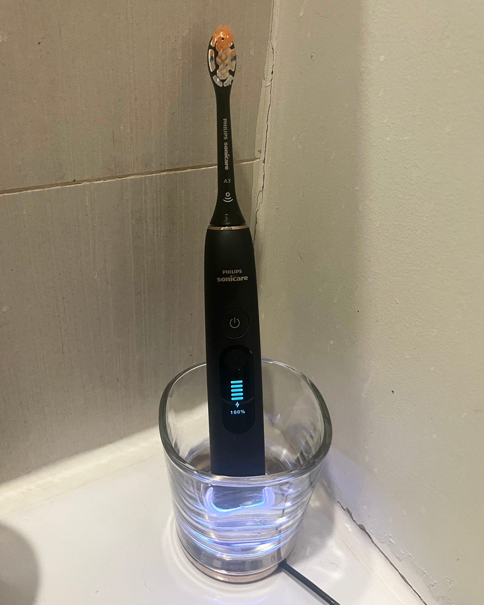 A black Philips Sonicare toothbrush in a glass charging holder next to a wall.
