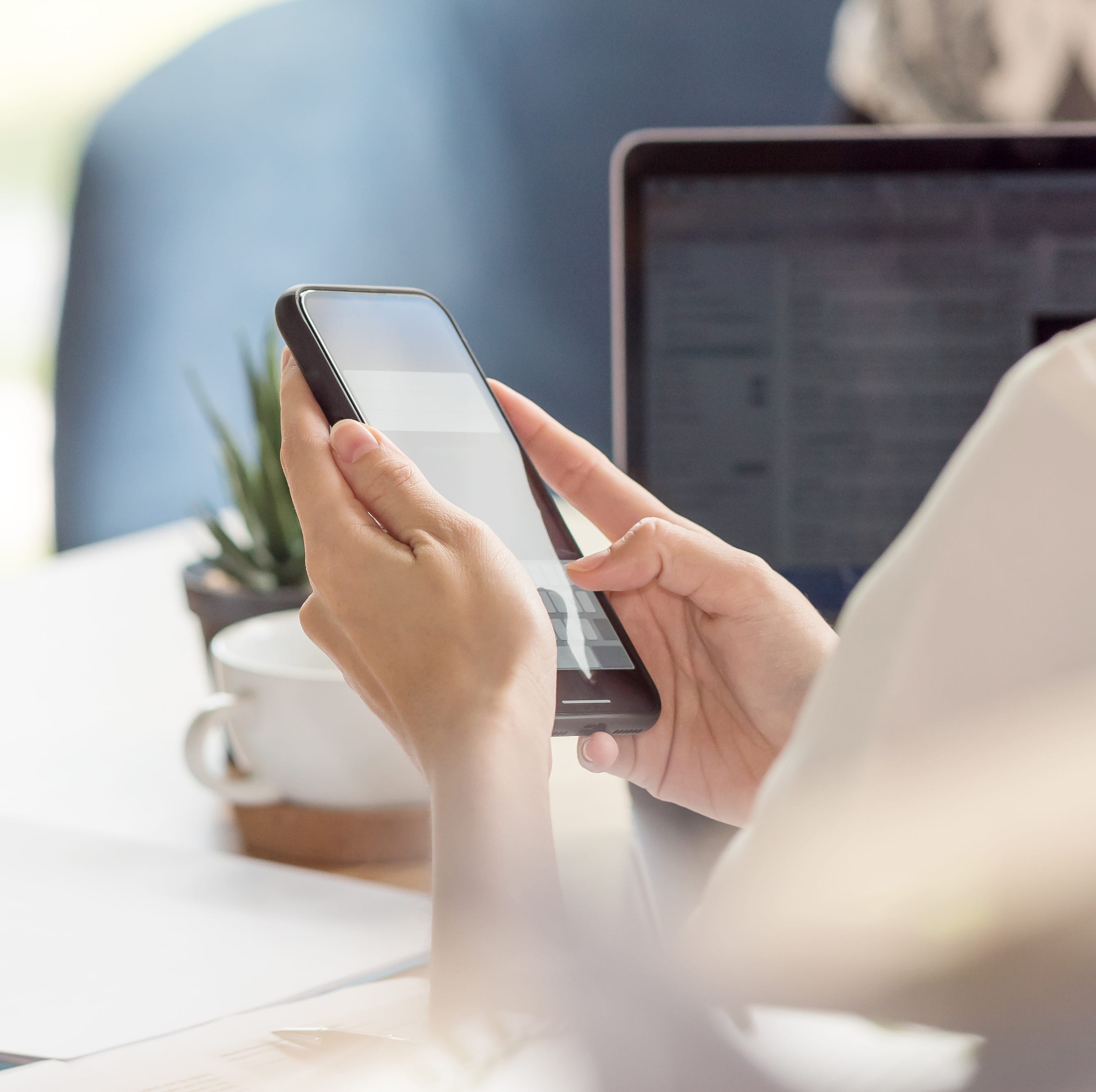 Female hand using smartphone while working at desk in office